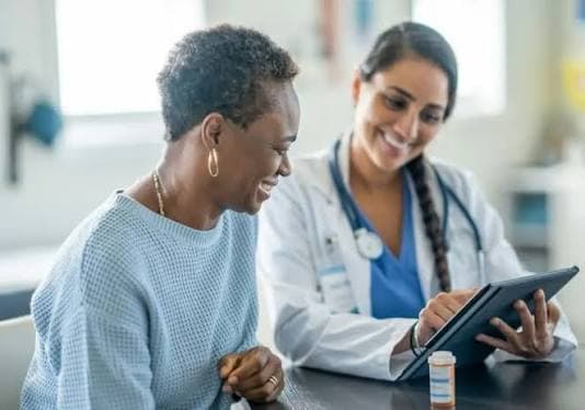 Physiotherapist showing a patient her results on a tablet, both smiling during a positive clinical conversation